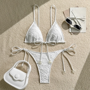 Flat lay of white textured bikini set with halter top and tassel ties on sand background