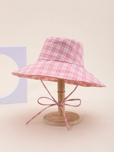 Detail of pink plaid bucket hat with wide brim and matching fabric bow on wooden stand