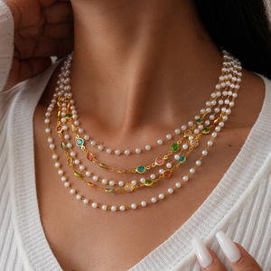 Multilayer gold necklace with colorful gemstones and pearls worn over a white sweater