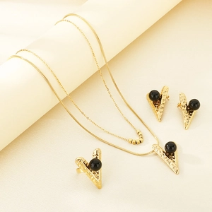 Detail of gold jewelry set with black spherical stones on a beige textured background