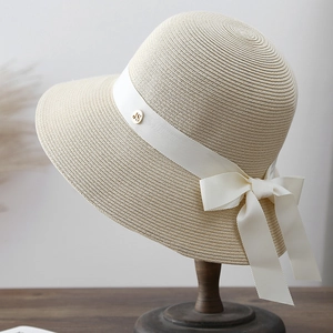 Détail d'un chapeau en paille beige avec ruban gros-grain blanc et logo en métal doré