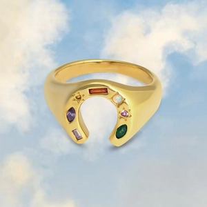 Dettaglio anello a ferro di cavallo dorato con pietre preziose colorate e opali su sfondo cielo