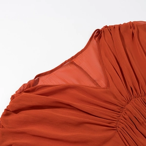 Detalle del escote en V de un vestido bohemio de gasa rojo anaranjado plisado