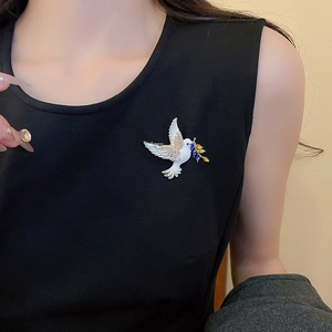 Detail of elegant white enamel dove brooch with gold olive branch on a black top