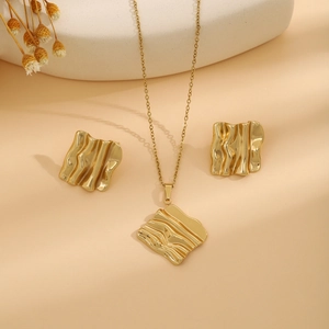 Detail shot of golden jewelry set featuring irregular wave texture on square pendants