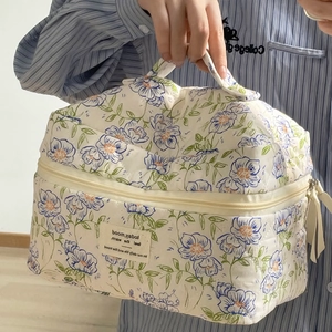 Detail of blue floral quilted makeup bag featuring top handle and beige fabric label