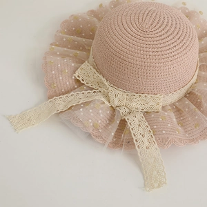 Vue détaillée d'un chapeau de paille rose pour enfant avec nœud en dentelle.