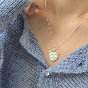 Dettaglio collana in argento 925 con ciondolo irregolare su maglione blu elegante