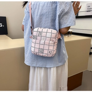 Pink checkered crossbody bag with Good Luck text shown on model in a modern cafe setting