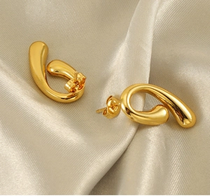 Macro di orecchini a goccia dorati lucidi disposti su un elegante tessuto di seta champagne