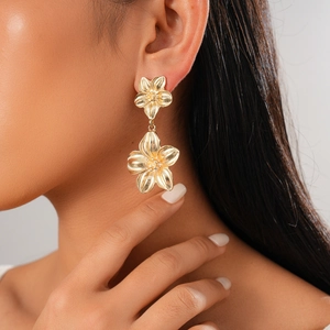 Close-up of a double-layered golden flower earring worn by a model in soft lighting