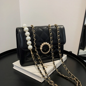 Detail of black quilted chain bag featuring large pearl pendant and golden hardware accents