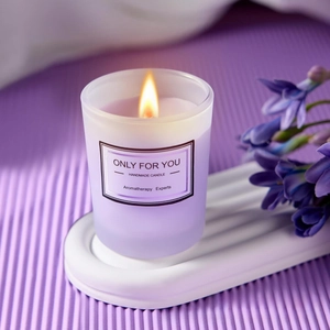 Close-up of a burning handmade aromatherapy candle in a frosted purple glass jar