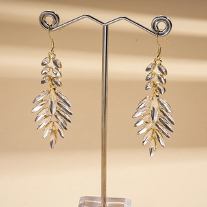 Macro detail of gold leaf earrings with clear crystals hanging on a metal display stand