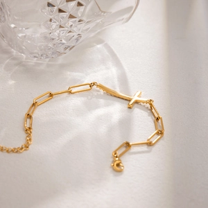 Close-up van gouden paperclip kettingarmband met een fonkelende kruisvormige hanger