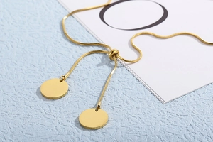 Detailed close-up of golden snake chain bracelet with polished round tags and slider clasp