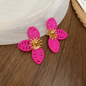 Close-up of pink woven flower earrings with golden stamens on a textured wood surface