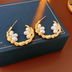 Detailed macro shot of C-shaped gold textured earrings with elegant white faux pearls