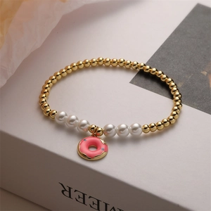 Dettaglio di un bracciale con perline dorate, perle bianche e ciondolo ciambella