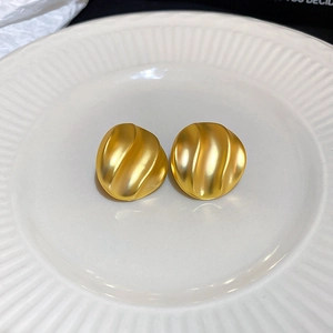 Dettaglio di orecchini tondi ondulati in oro opaco su piatto di ceramica bianca