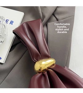 Detail of burgundy ruched leather handle and glossy gold oval metal hardware on handbag