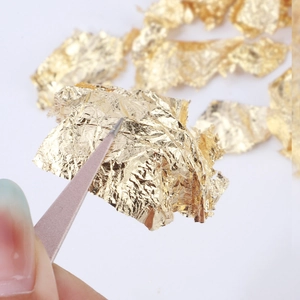 Shinny gold leaf flakes for cake decoration and nail art being picked up by pink tweezers