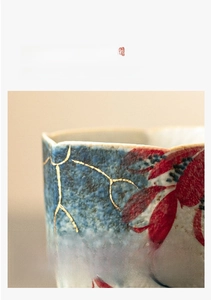 Macro shot of blue ceramic tea cup featuring gold lines and red flower petal patterns