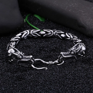 Detailed shot of men's stainless steel dragon head bracelet on dark pebbles with a small leaf