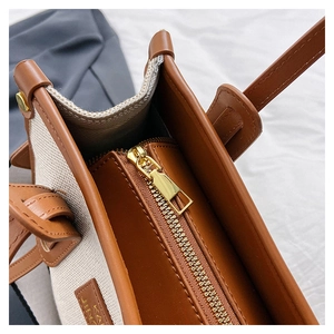 Detailed close-up of brown leather and beige canvas tote bag with durable metal zipper