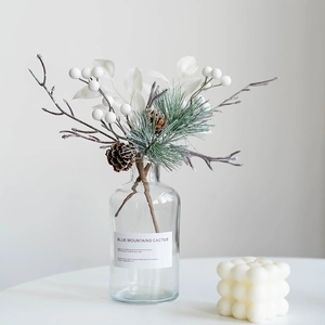 Christmas decoration with pine cones and white berries in a glass vase on a white table