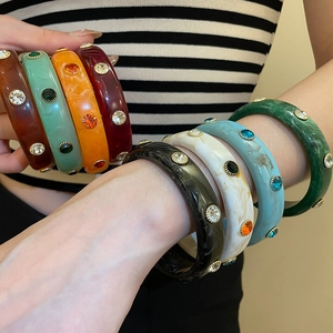 Detail view of colorful acrylic bangles set with sparkling rhinestones on model wrist