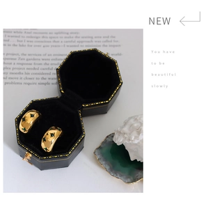 Detailed view of C-shaped gold earrings with green zircon in a black jewelry box