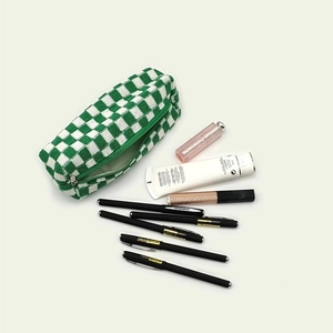 Close-up of green and white checkered knit pouch with stationery and cosmetics items