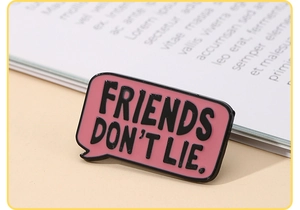 Detail of pink speech bubble enamel pin with Friends Don't Lie text on a book