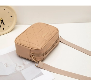 Detailed view of beige quilted cross-body bag with double zippers and wide fabric strap