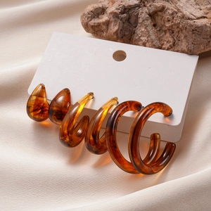 Detail of amber acrylic earring set featuring teardrop and spiral shapes on silk fabric