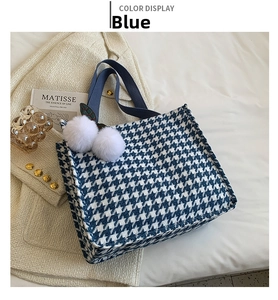 Detail of blue houndstooth tote bag featuring white pom-pom charms and dark blue handles