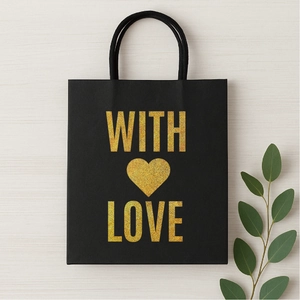 Close-up of black gift bag with gold glitter WITH LOVE text and heart on wooden background