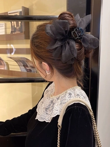 Close-up of a large black organza bow hair claw clip worn by a model in a bun