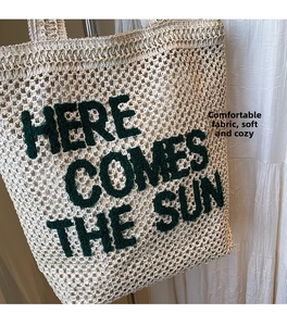 Detail of woven tote bag with green plush Here Comes The Sun slogan on creamy white fabric