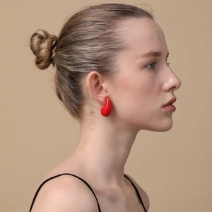 Chic red teardrop-shaped stud earring with polished finish worn by a female model