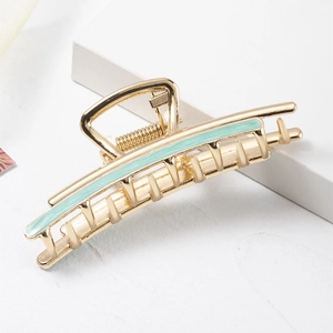 Detail view of large golden hair claw clip with light green enamel inlay on white background