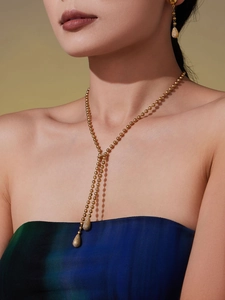 Détail d'un collier en Y à perles dorées 18k avec boucles d'oreilles pendantes assorties