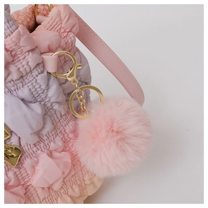 Close-up of pink gradient pleated fabric bag with gold hardware and plush ball detail