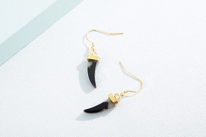Détail de boucles d'oreilles dorées avec pendentifs corne noir et blanc sur fond texturé