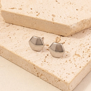 Macro shot of silver hexagonal stud earrings on natural beige travertine stone texture