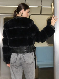 Short black faux fur jacket with leather trim shown on model in a subway station