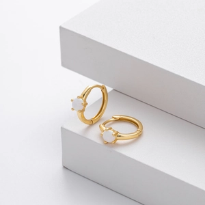 Detailed close-up of gold huggie hoop earrings with round white opal stones on white background