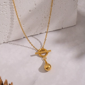 Detail of golden water drop pendant with OT toggle clasp on a textured stone surface
