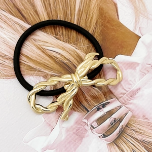 Minimalist black hair tie with golden woven metal bow charm on a stylish magazine background